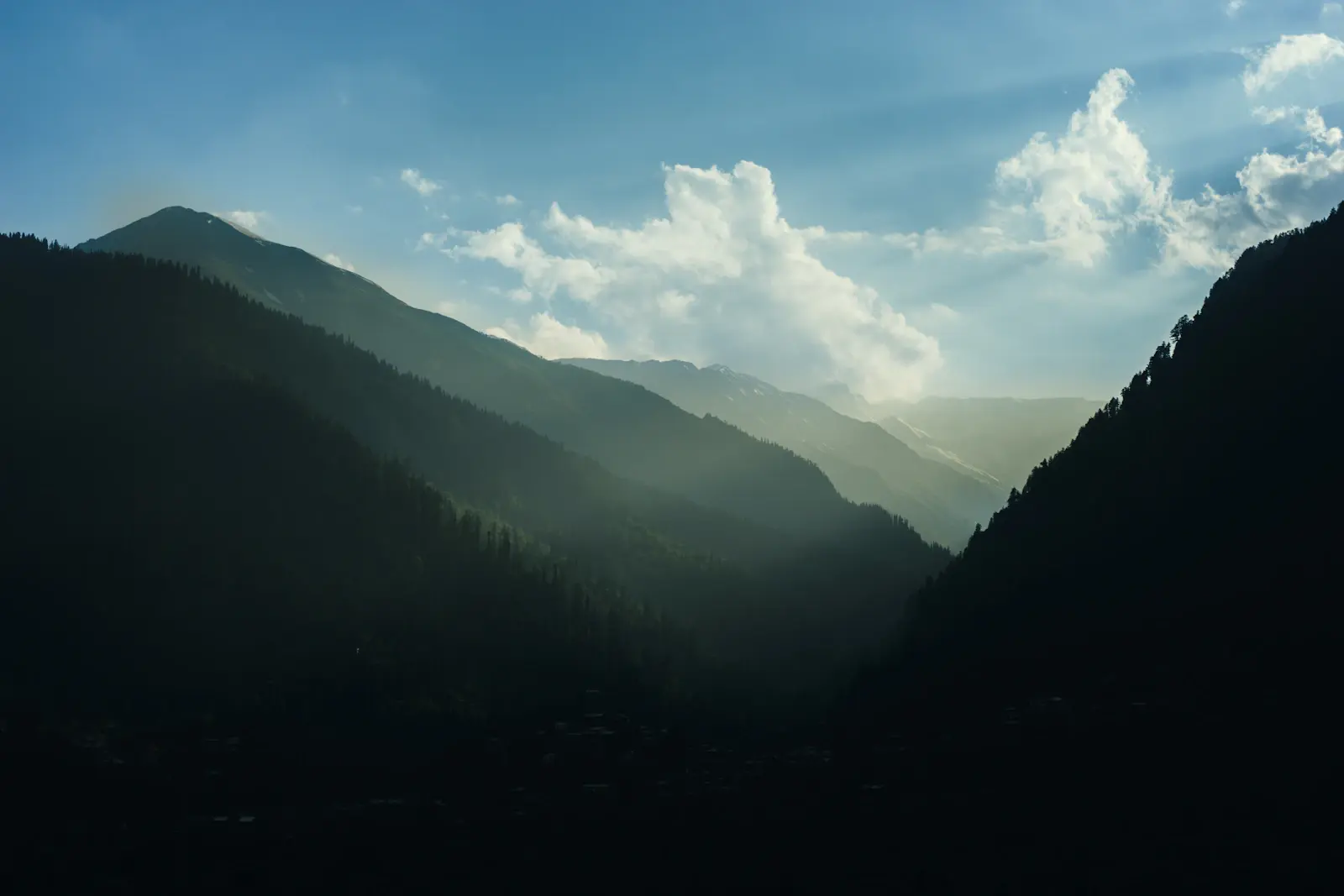 Sunlight falling between forested mountain ridges in Manali